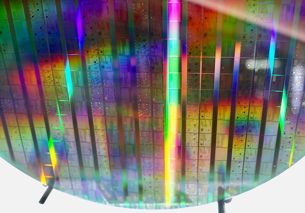 A full silicon wafer of Intel's commercial quantum computing processor on display. Multicolored sheen to the surface is present created by the microstuctures achieved by the lithographic etching process.