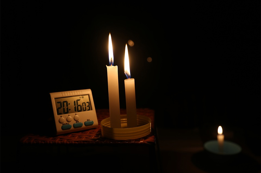 Three lit candles in a dark room with one almost fully melted and a digital clock displaying the time as 20:16:03.