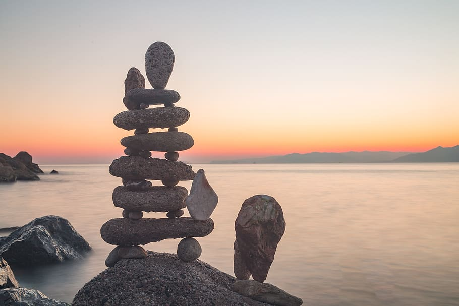 Photograph of many pebbles stacked make a tower near the ocean at dawn.
