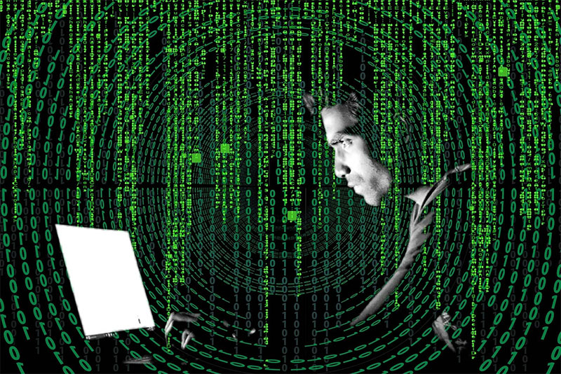 Image of a cybercriminal using his laptop for attempting cyberattacks with a binary background.