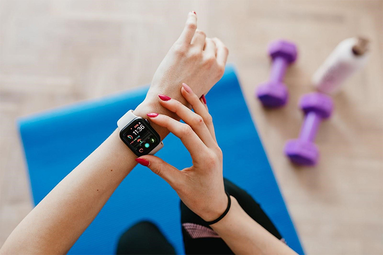 a woman using her apple watch at a workout while on a yoga mat with 2 dumbbells next to her.
