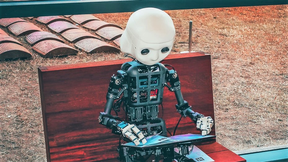 Image of a robot sitting on a bench with a tablet in hands.