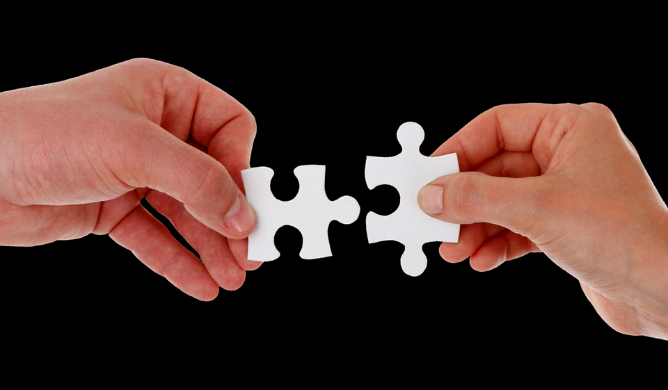 Image of two hands holding two pieces of jigsaw puzzles respectively and trying to connect them.