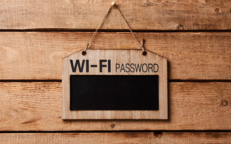 Image of a brown wooden sign hanging from a wooden wall. The sign has the words "WI-FI PASSWORD" positioned above a black rectangle.