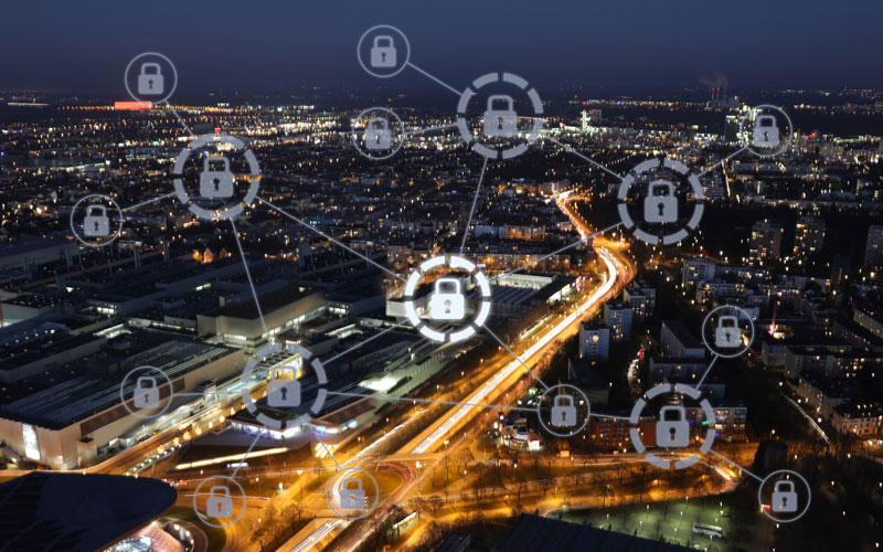 A graphic image of a network of grey padlocks superimposed on a cityscape at night. Each padlock is enclosed by a circle. A single road with light trails runs diagonally across the center of the image.