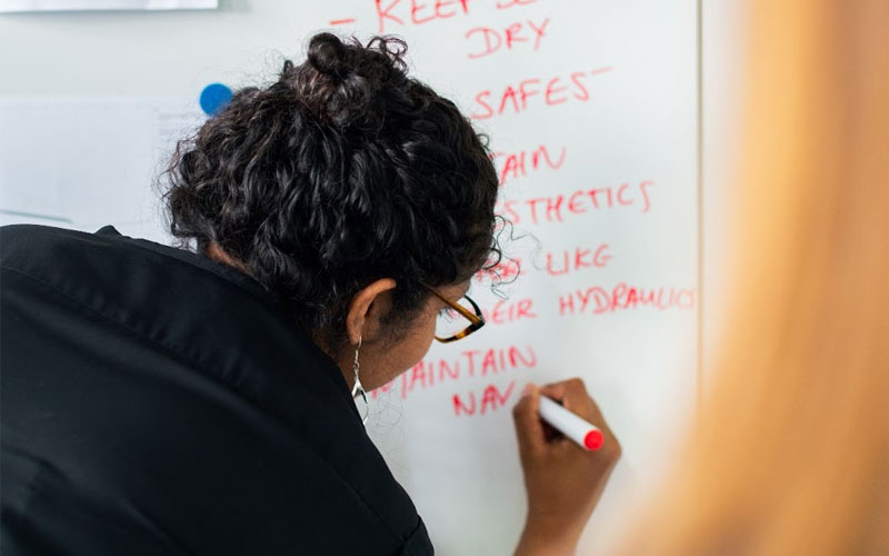 Image of a woman writing on a white board about creating resilient systems.