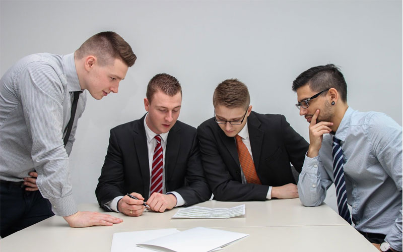Image of a group of employees gathered around a desk analyzing a paper.
