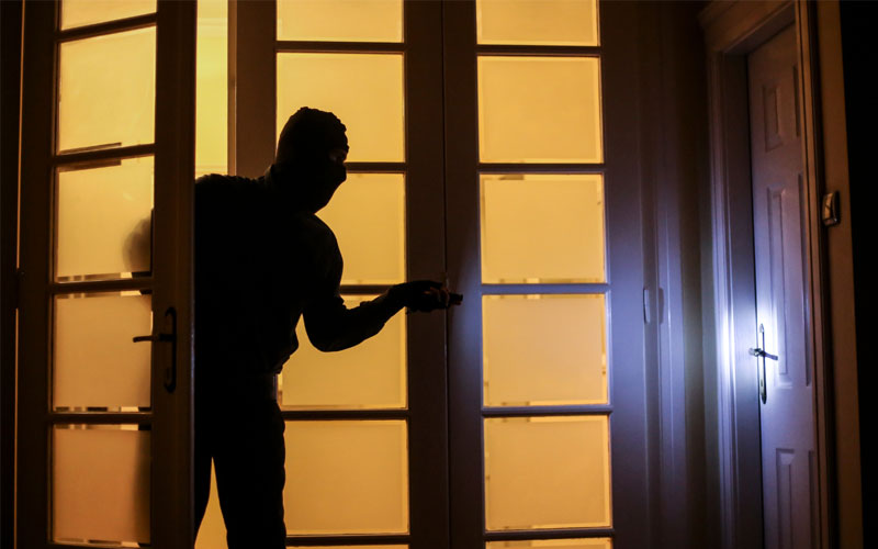 Image of an intruder. It shows a silhouette of a person breaking into a room, backdropped by yellowish orange lighting.