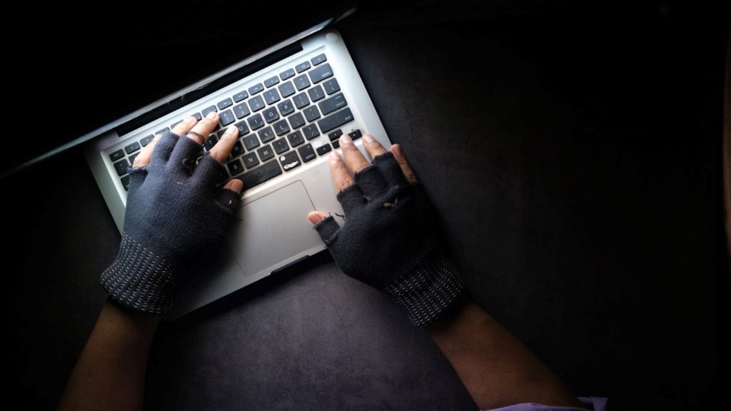 Image of a man wearing black fingerless gloves typing on a laptop.