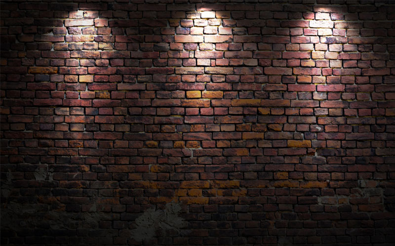 a brick wall with three lights shining from the top. bricks are in different shades of brownish red and orange