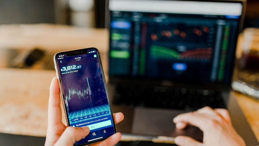 Image of a person using a phone and laptop with trading and investment apps.