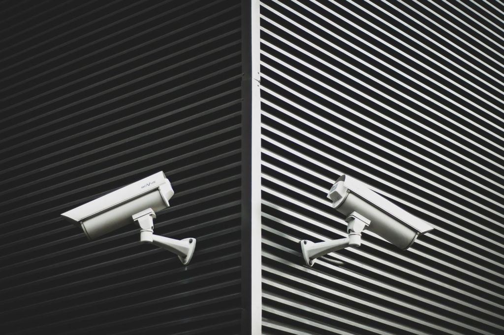Image off a corner of a building, where two security cameras are looking in opposite directions while the contrast of the building is darker on the left and lighter on the right.
