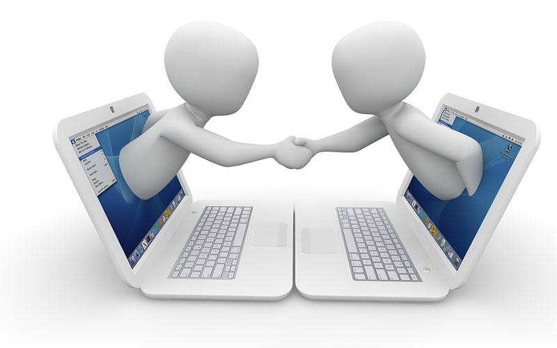 Image of two humanoids shaking hands from computers placed opposite each other.