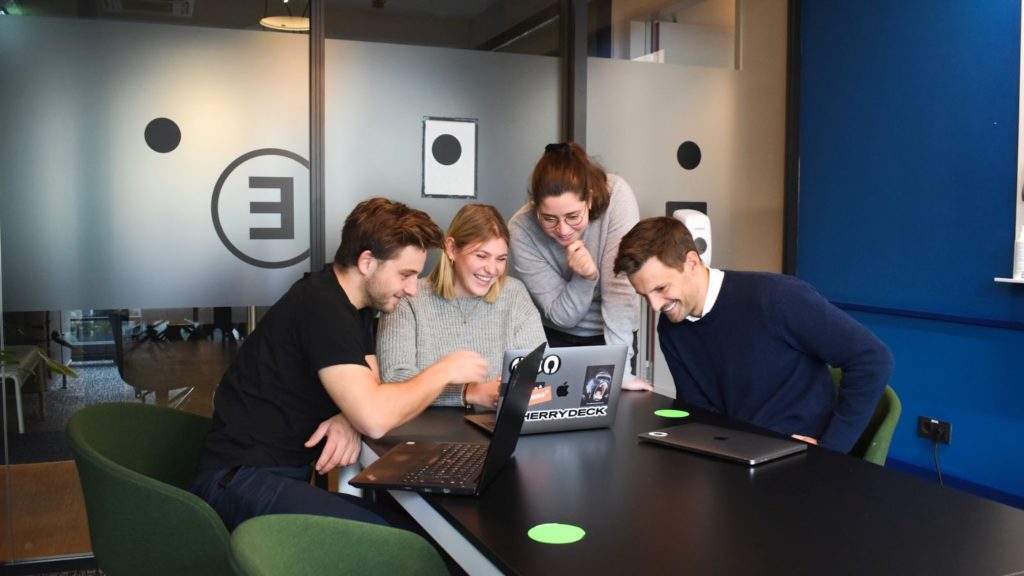 Image of four people standing and laughing at the office about something on the laptop screen.