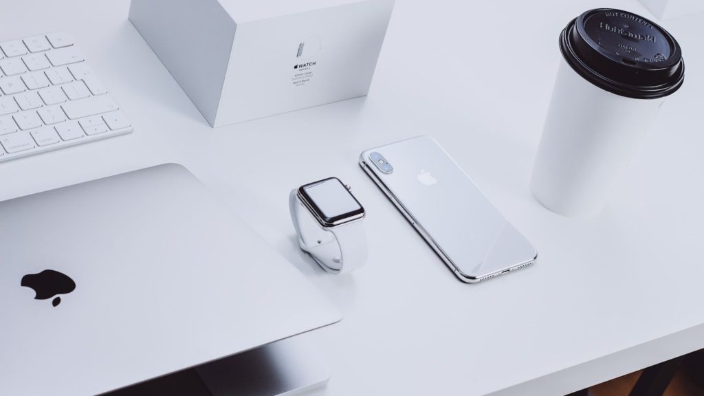 Apple products including a MacBook, Apple watch, and iPhone on a white desk.