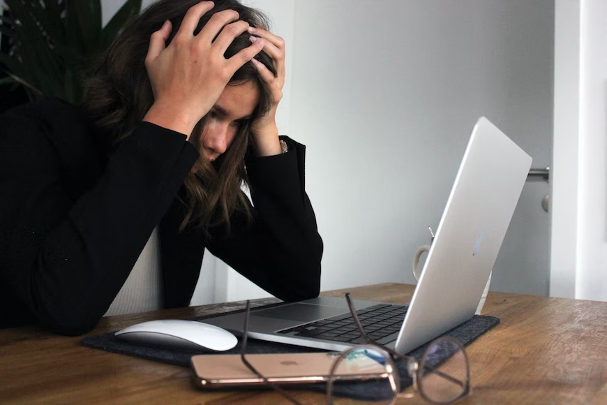 An image of a woman with her head in her hands, looking at a laptop screen in frustration.