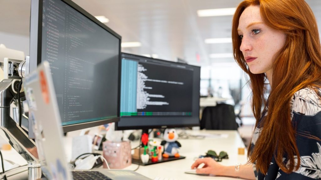 Image of a woman coding on two computer screens.