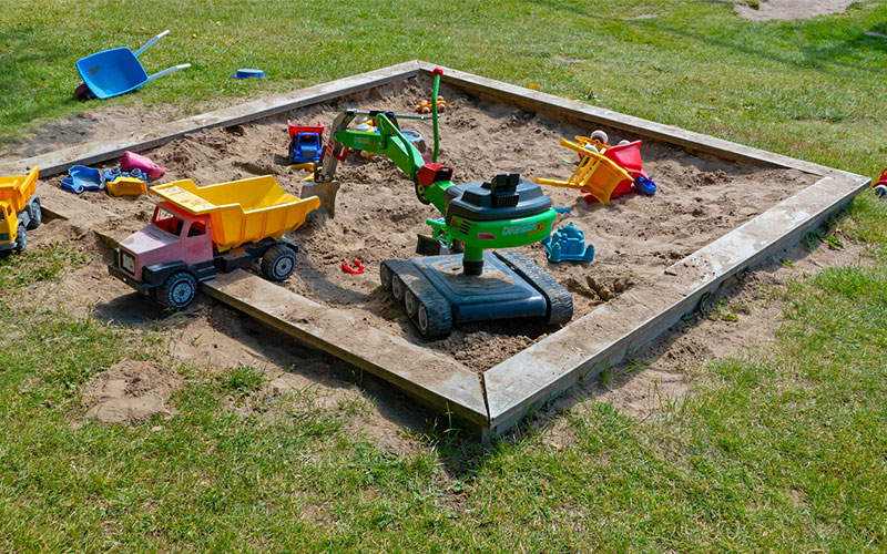Image of a sandbox with toys scattered around it.
