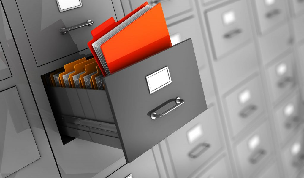 An image of an open filing cabinet with multiple files inside. A red folder protrudes from the draw.