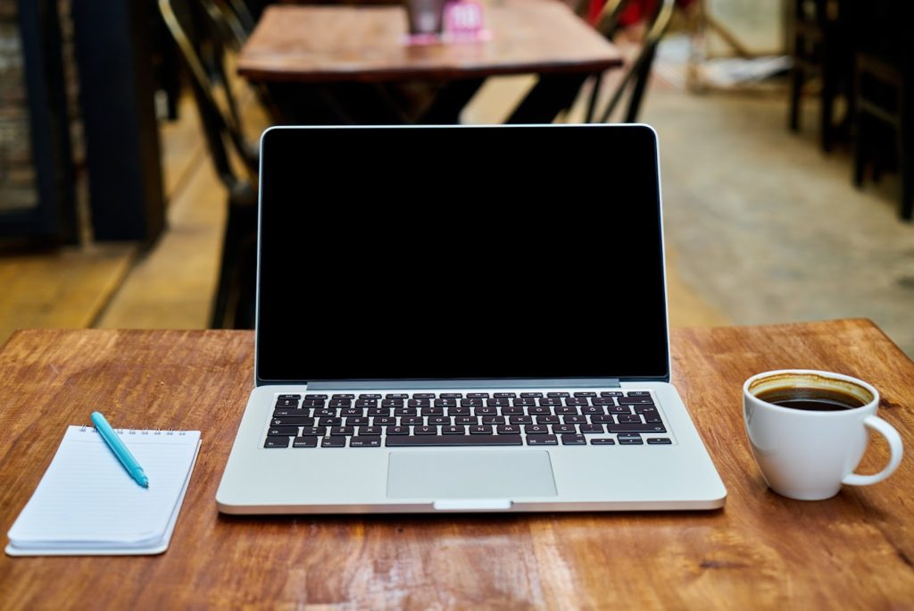 Image of a laptop with a notepad to the left and a cup of coffee to the right.