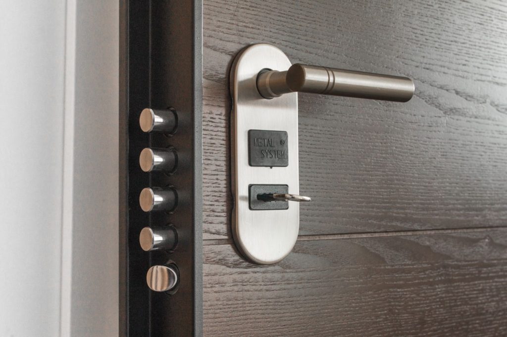 Image of a silver door lock with a key inside and 4 bolts, against a wooden frame.