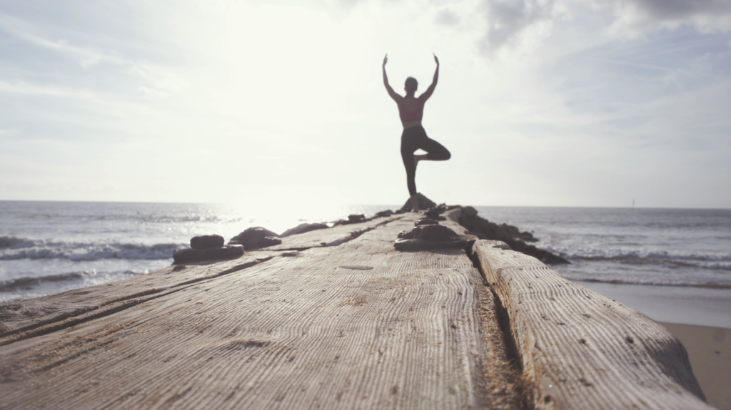 Image of a person doing yoga on a beachhead. 