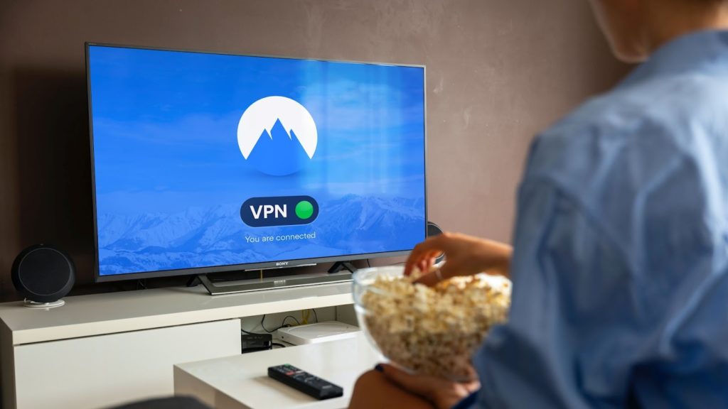 Image of a person watching at a TV with a NordVPN logo and eating popcorn.