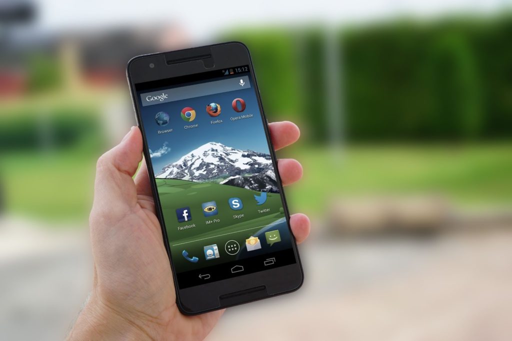The image shows a hand holding an Android phone against a blurred background