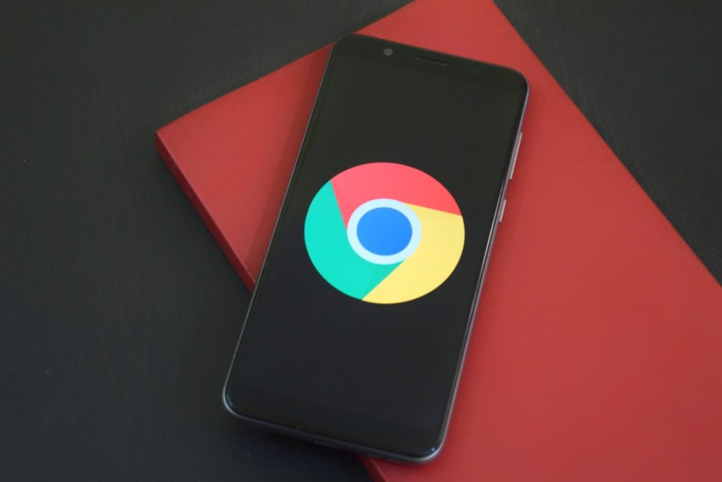 The image shows a black smartphone on a red notebook, displaying Google's logo on the screen.