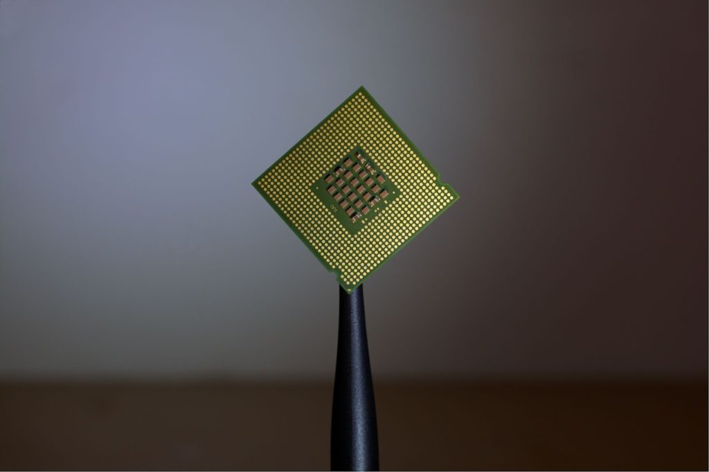 The image shows a single green and yellow microchip held in the center against a dark-grey background.