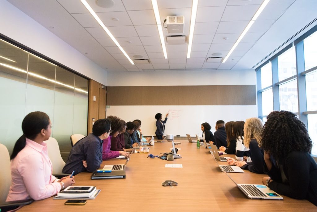 The image shows a meeting room with employees attending a presentation.