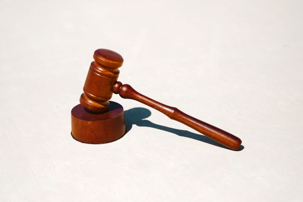The image shows a small gavel resting on a mallet against a cream-white background. 