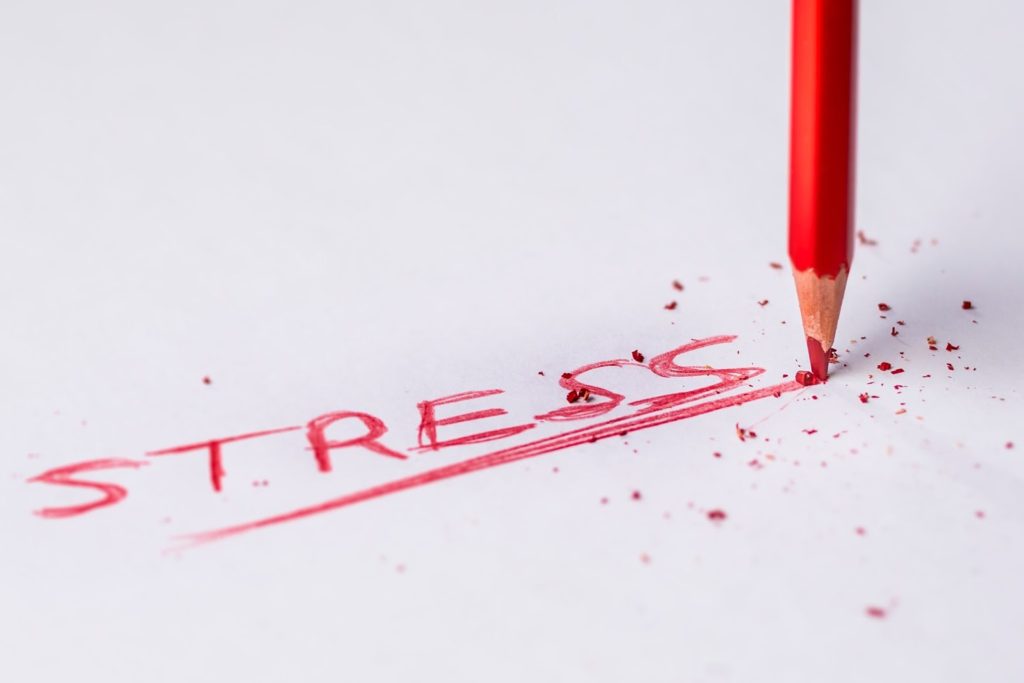The image shows a red coloring pencil, writing out the word "stress" on a white surface.
