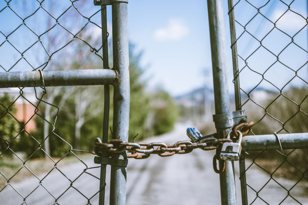 The image shows a rusty chain with locks, holding a fence wire gate together.