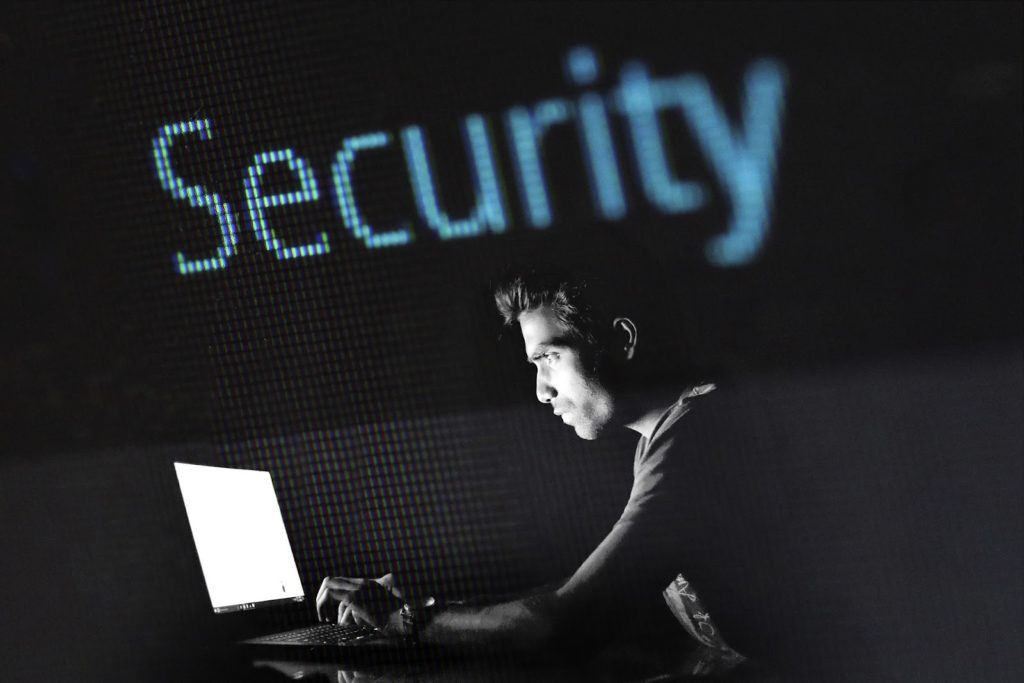 A man in a dark room on a laptop, with the word "security" above him.